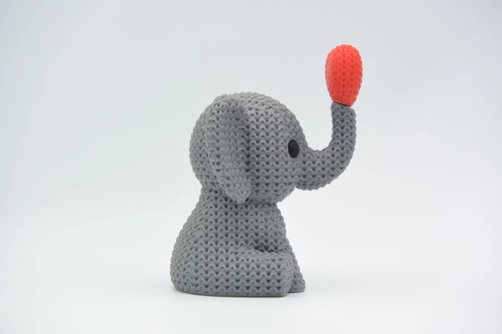 Grey coloured knitted textured 3D printed Elephant with heart figure/ key tag on a white background facing sideways 